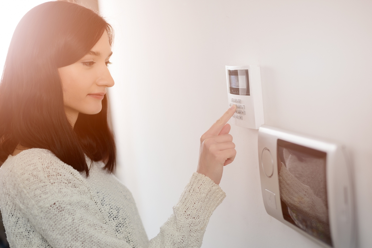 Young brunette woman entering code on keypad of home security alarm. Video intercom next to alarm keypad.