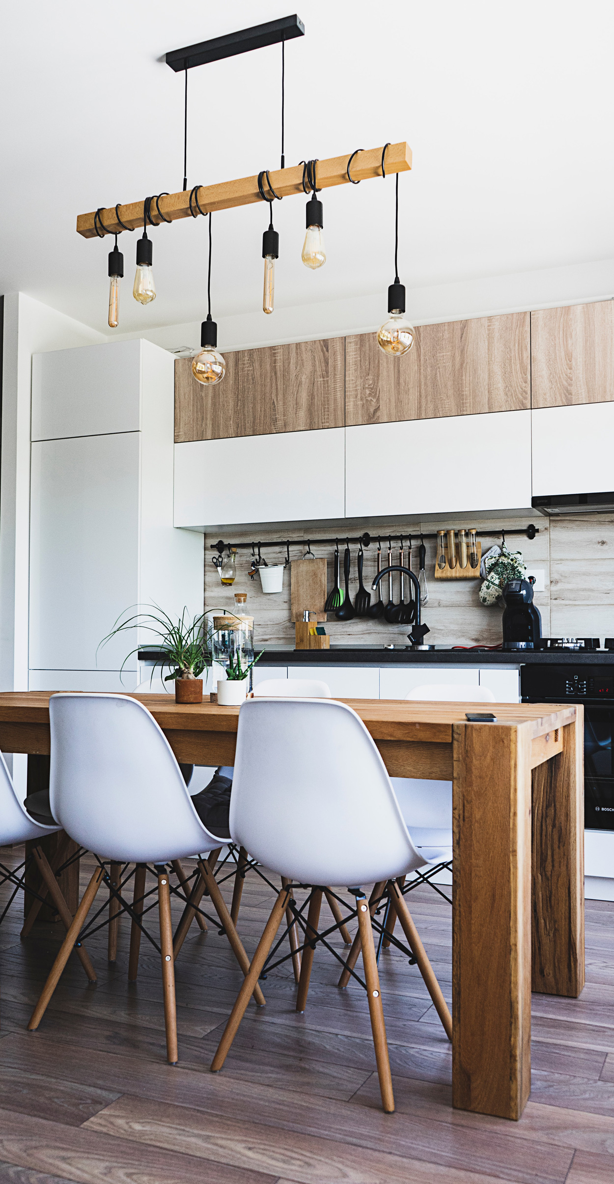 Woonkeuken met veel houten elementen, zwarte kranen en een grote robuuste eettafel.