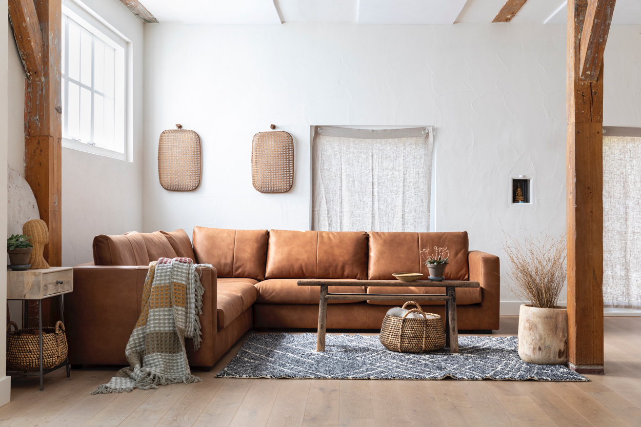 Landelijk interieur met een bruin lederen hoekbank met herkenbare, oude boerderij balken van een de vers gewitte hooischuur.