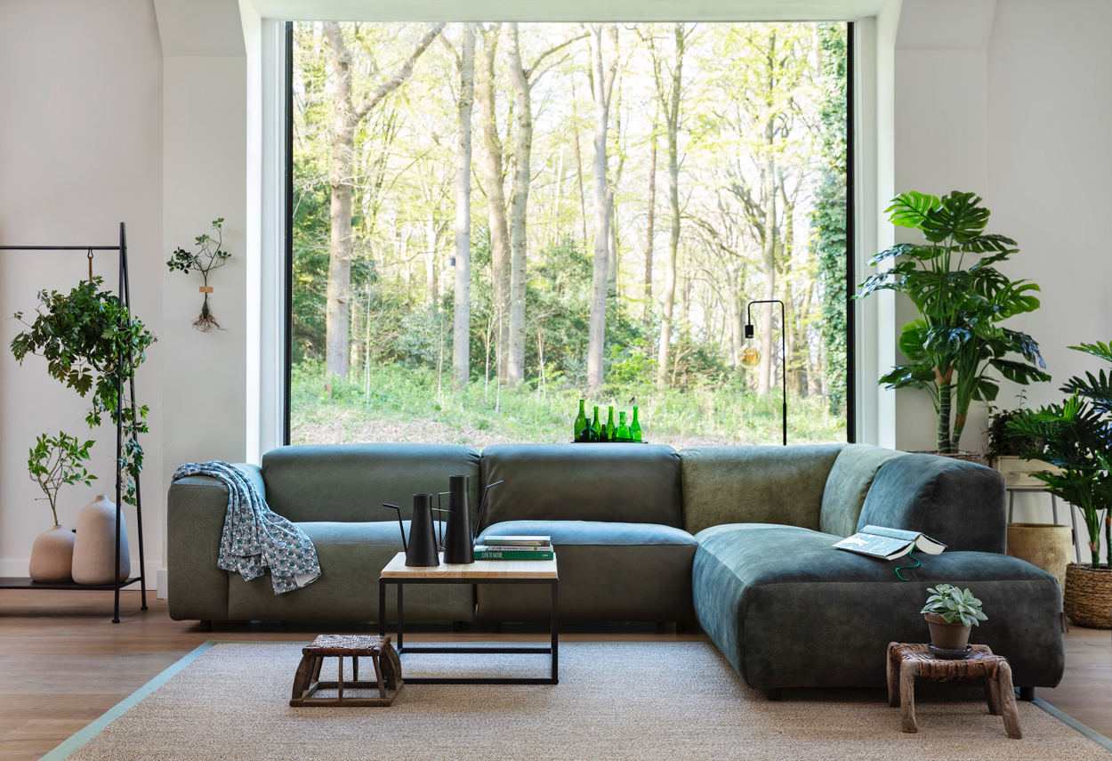 Prachtige modulaire bank in groen leder. Deze bankstel is onderdeel van een landelijk, greenhouse interieur met grote planten, aardetinten en houten decoratie.