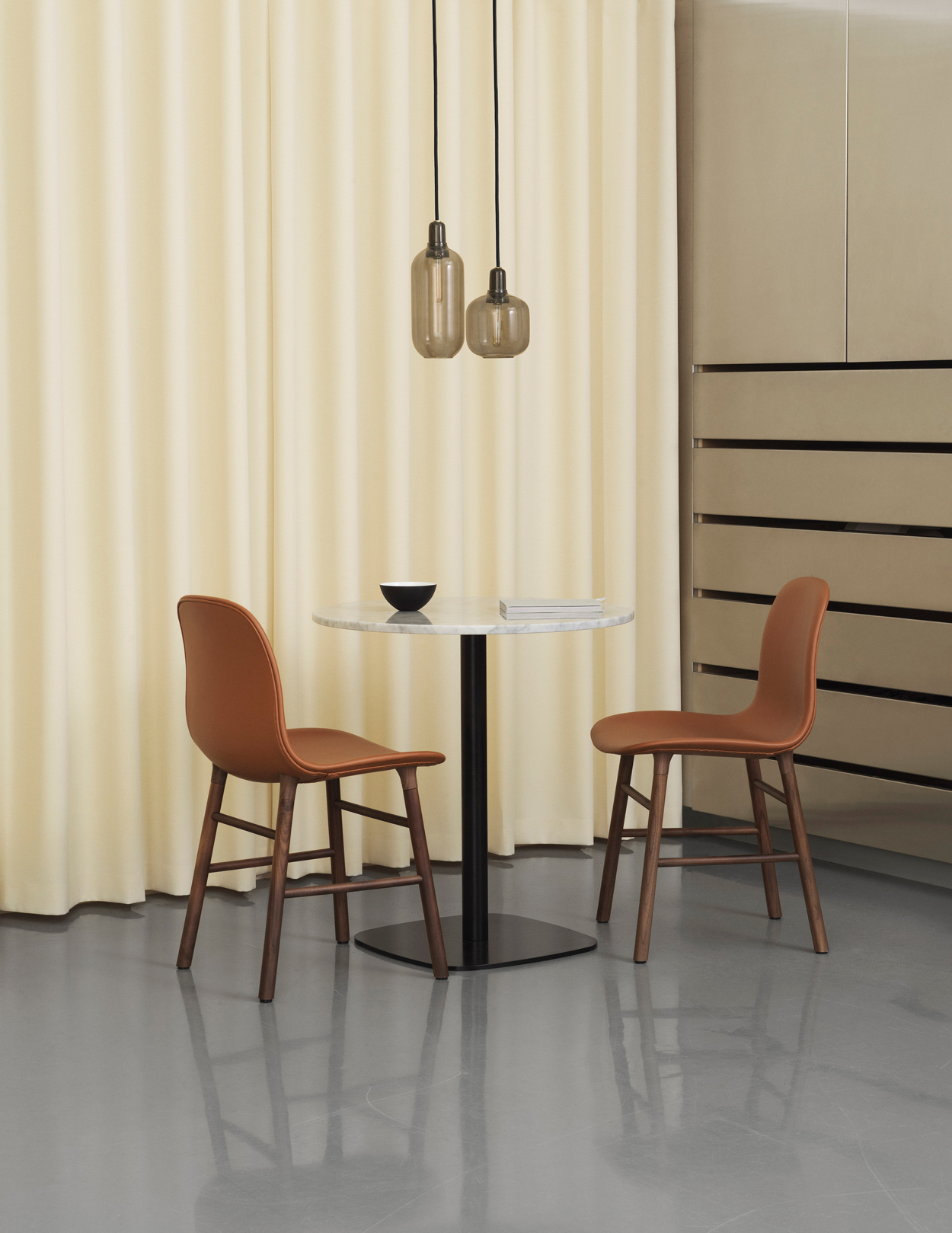 Twee moderne stoelen aan een marmeren, ronde tafel van het hippe bedrijf Normann Copenhagen. De zitschelp is bekleed met bruin leder.