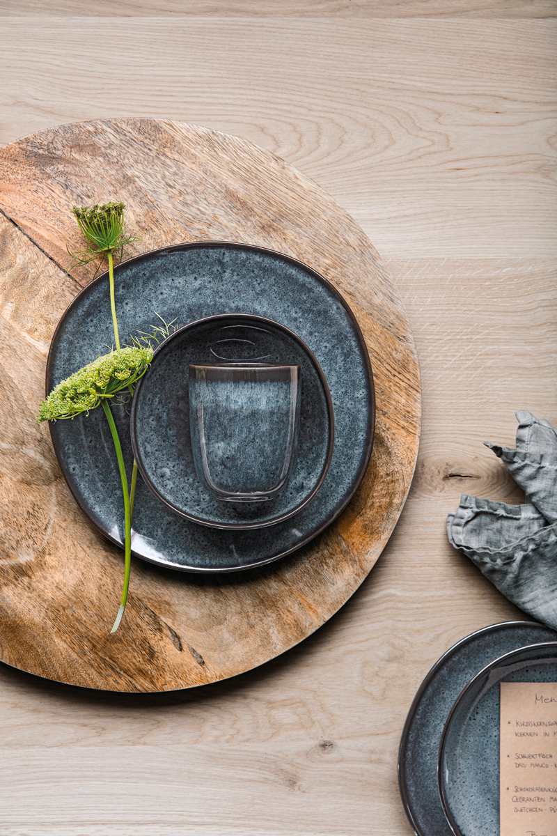 Een natuurlijk gedekte tafel met blauw-bruin servies bestaande uit borden, schalen en kopjes.